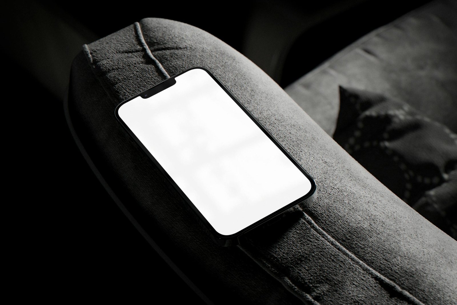 Close-up of a smartphone with blank screen placed on a couch armrest in low light conditions.